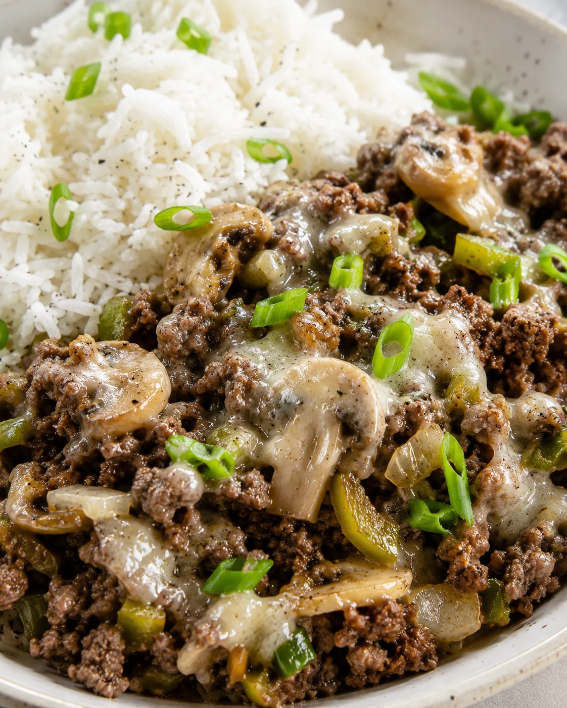 Close-up of Philly cheesesteak meal prep showing ground beef, mushrooms, peppers, melted cheese and basmati rice