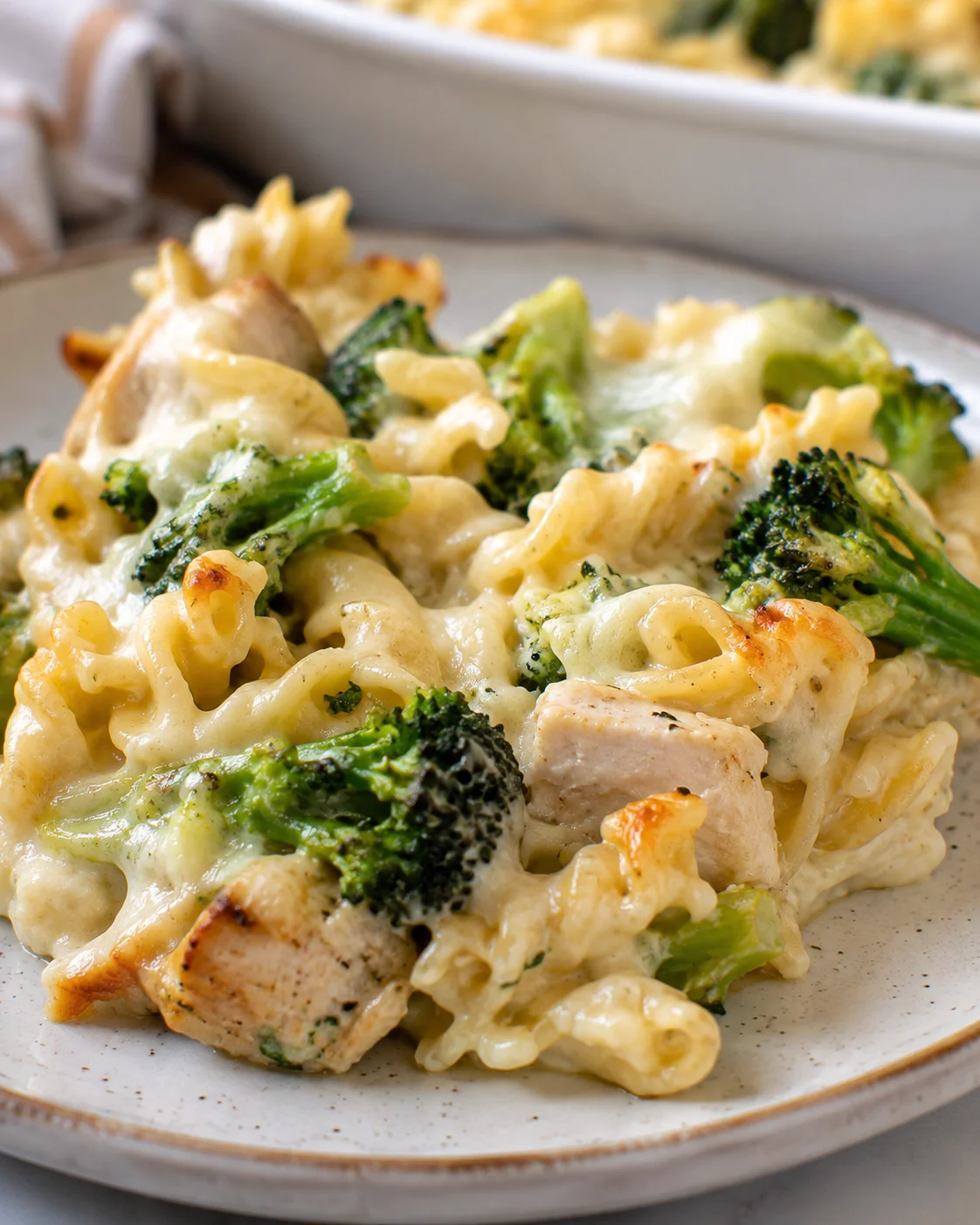 Plated serving of high protein chicken alfredo bake with broccoli and melted cheese on a ceramic plate