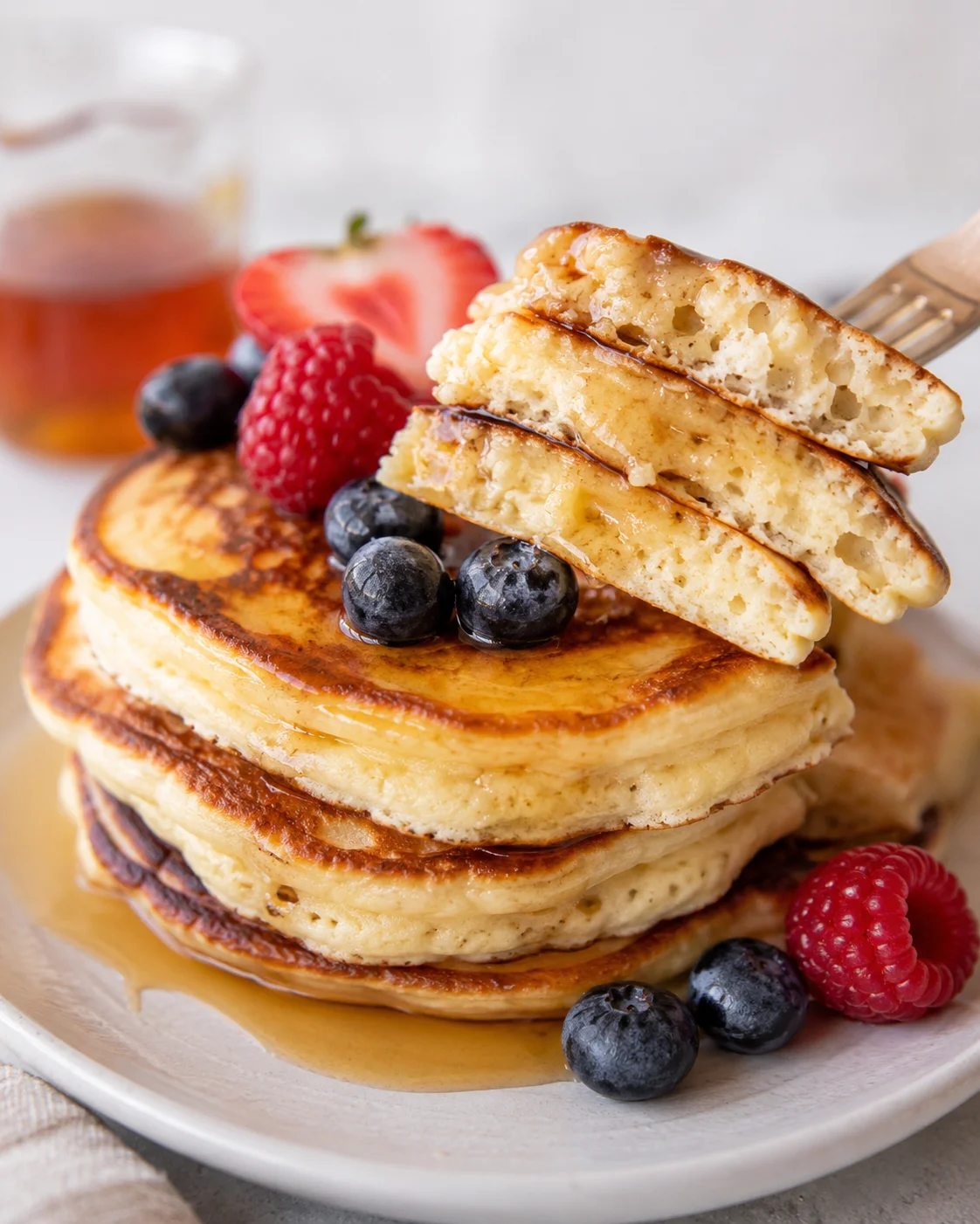 Fork lifting a bite of protein pancakes showing fluffy interior with berries and syrup