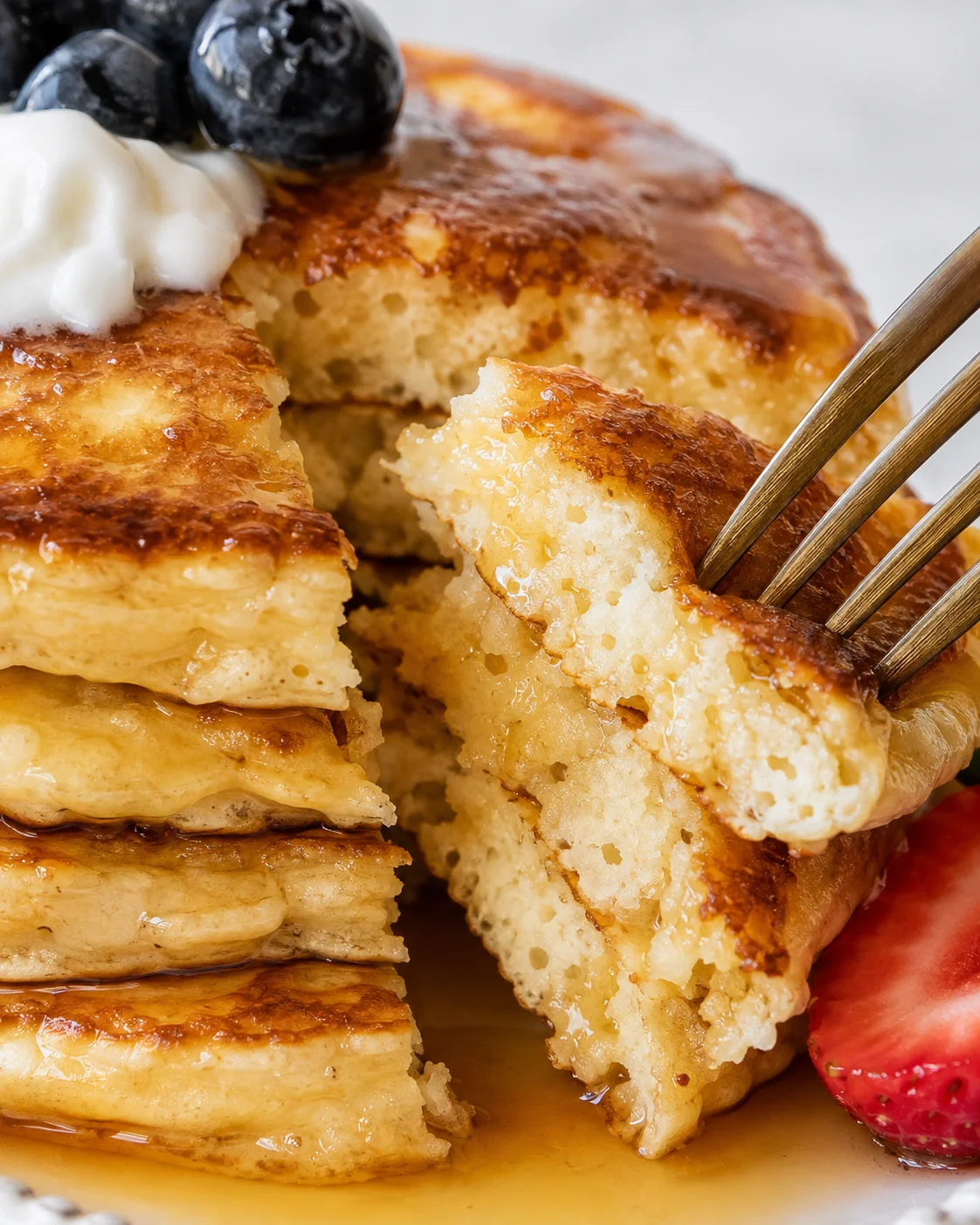 Close-up of a fork cutting into protein pancakes showing moist crumb and a dollop of Greek yogurt