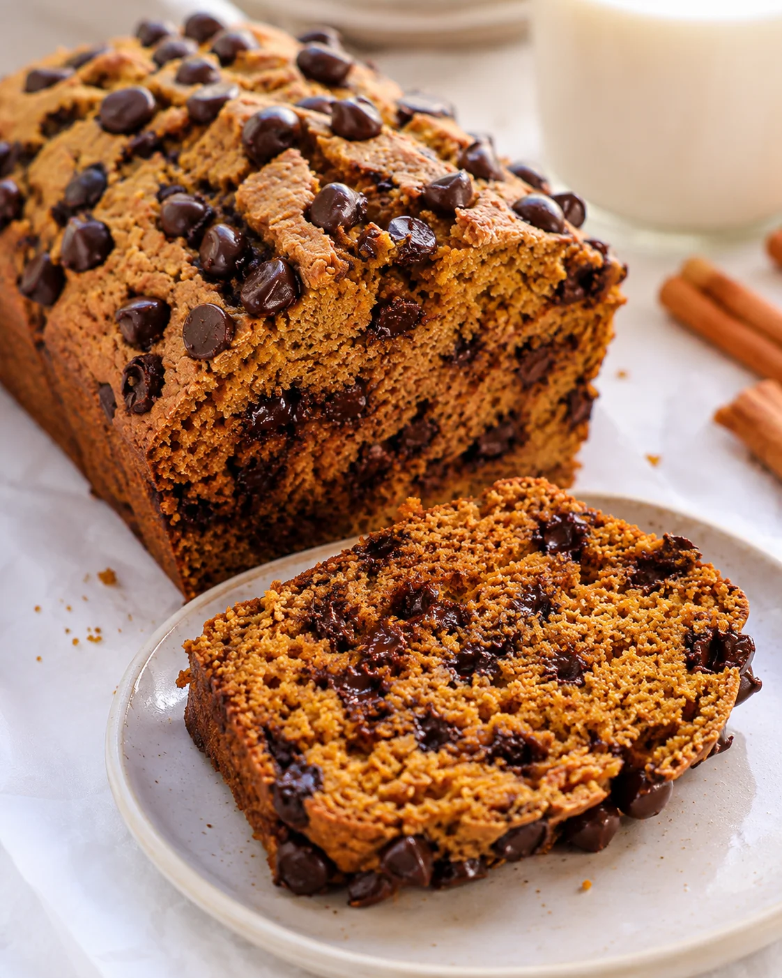 Protein pumpkin bread loaf with a sliced piece on a plate and a glass of milk