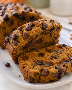 Two slices of protein pumpkin bread with chocolate chips on a plate and the remaining loaf in the background