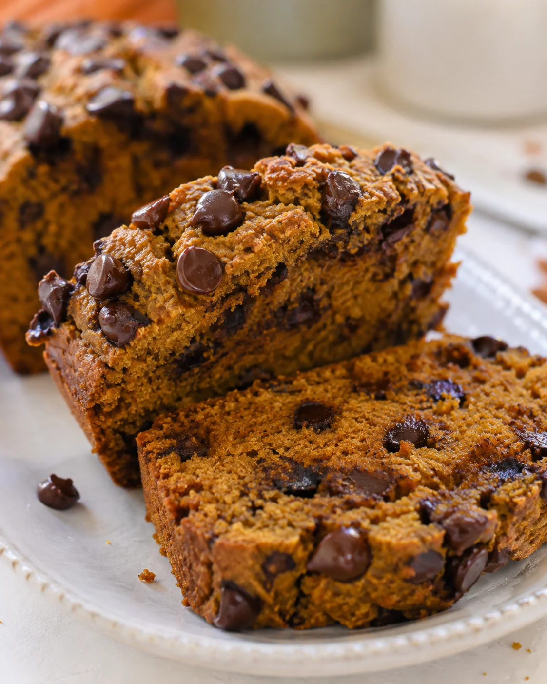 Two slices of protein pumpkin bread with chocolate chips on a plate and the remaining loaf in the background