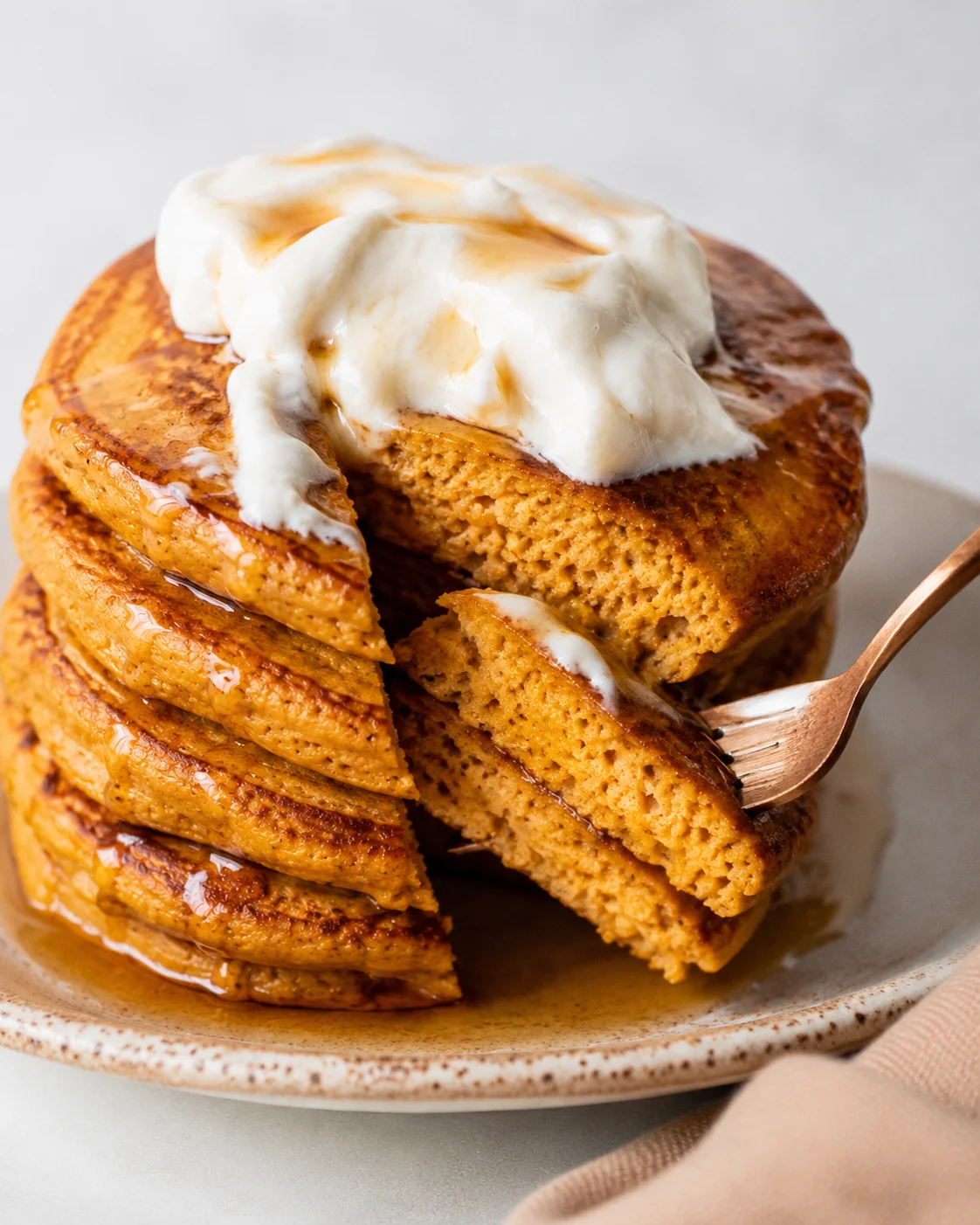 Pumpkin protein pancakes with a fork lifting a bite, showing the soft interior and syrup