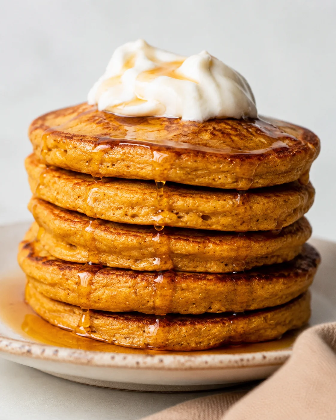 Stack of pumpkin protein pancakes topped with whipped yogurt and maple syrup
