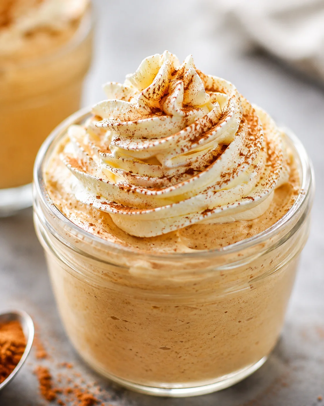 Close-up of pumpkin spice whipped Greek yogurt in a glass jar topped with piped cream and cinnamon