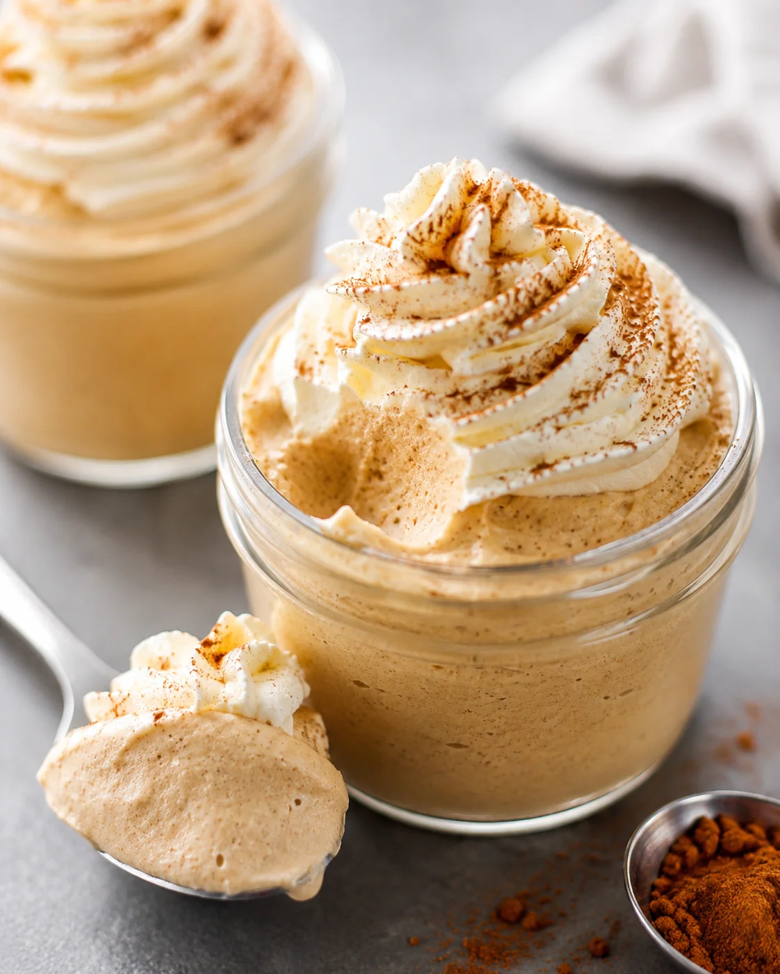 Jar of pumpkin spice whipped Greek yogurt topped with piped cream and cinnamon with a spoonful beside it