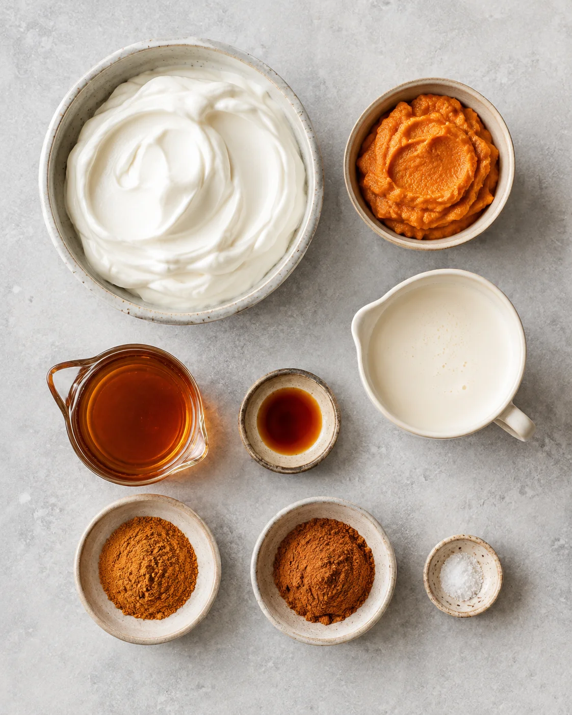Top-down view of ingredients for pumpkin spice whipped Greek yogurt: Greek yogurt, pumpkin puree, cream, maple syrup and spices