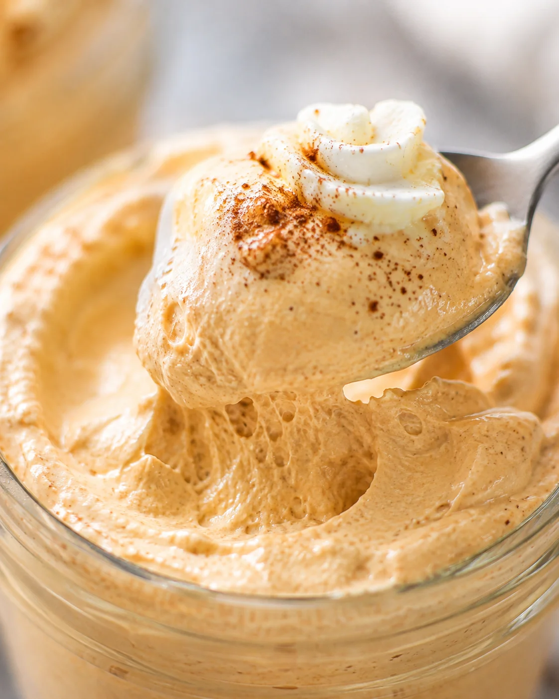 Spoon lifting a scoop of pumpkin spice whipped Greek yogurt showing airy, whipped texture