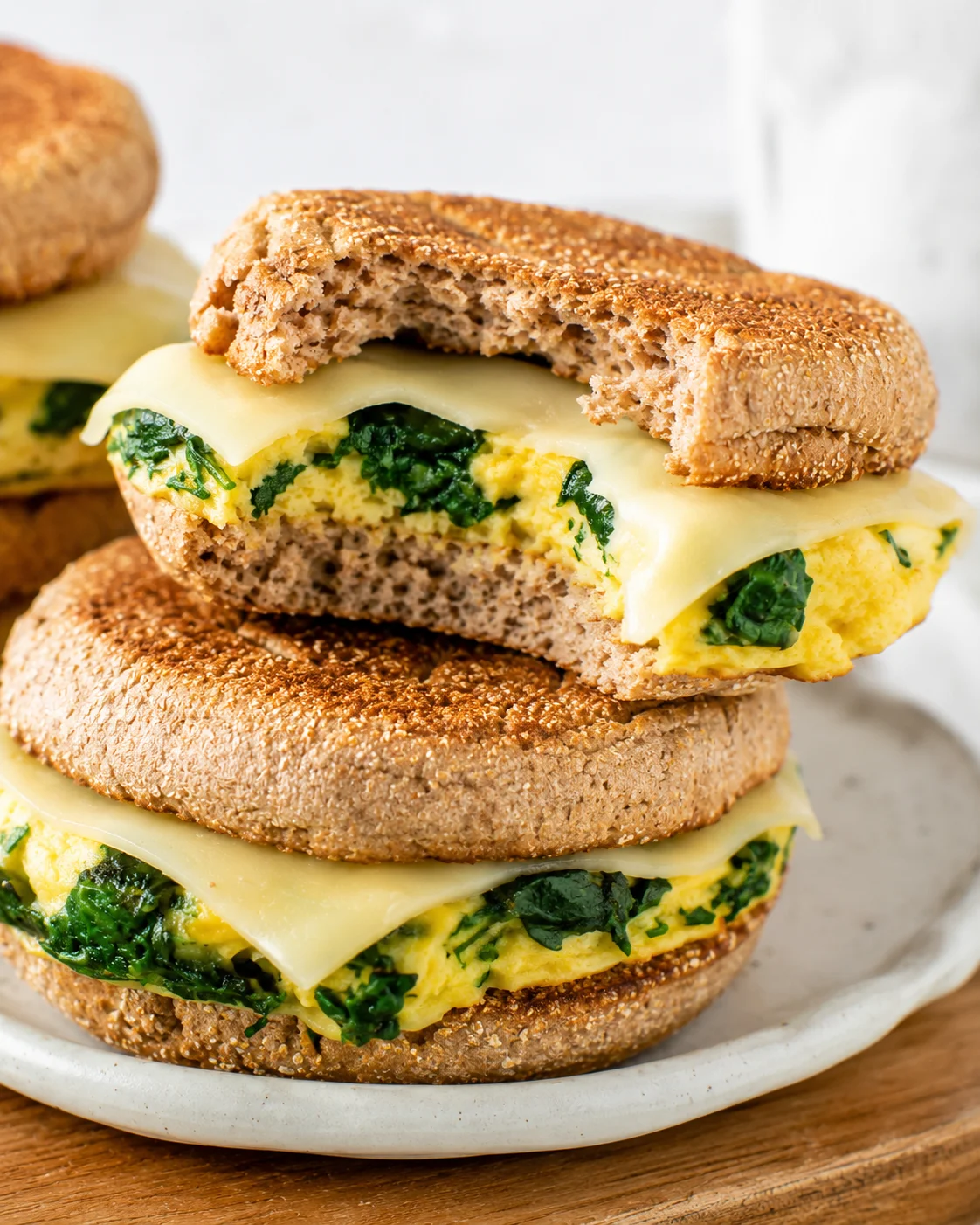 Spinach and egg breakfast sandwich with a bite taken to reveal the omelet and cheese