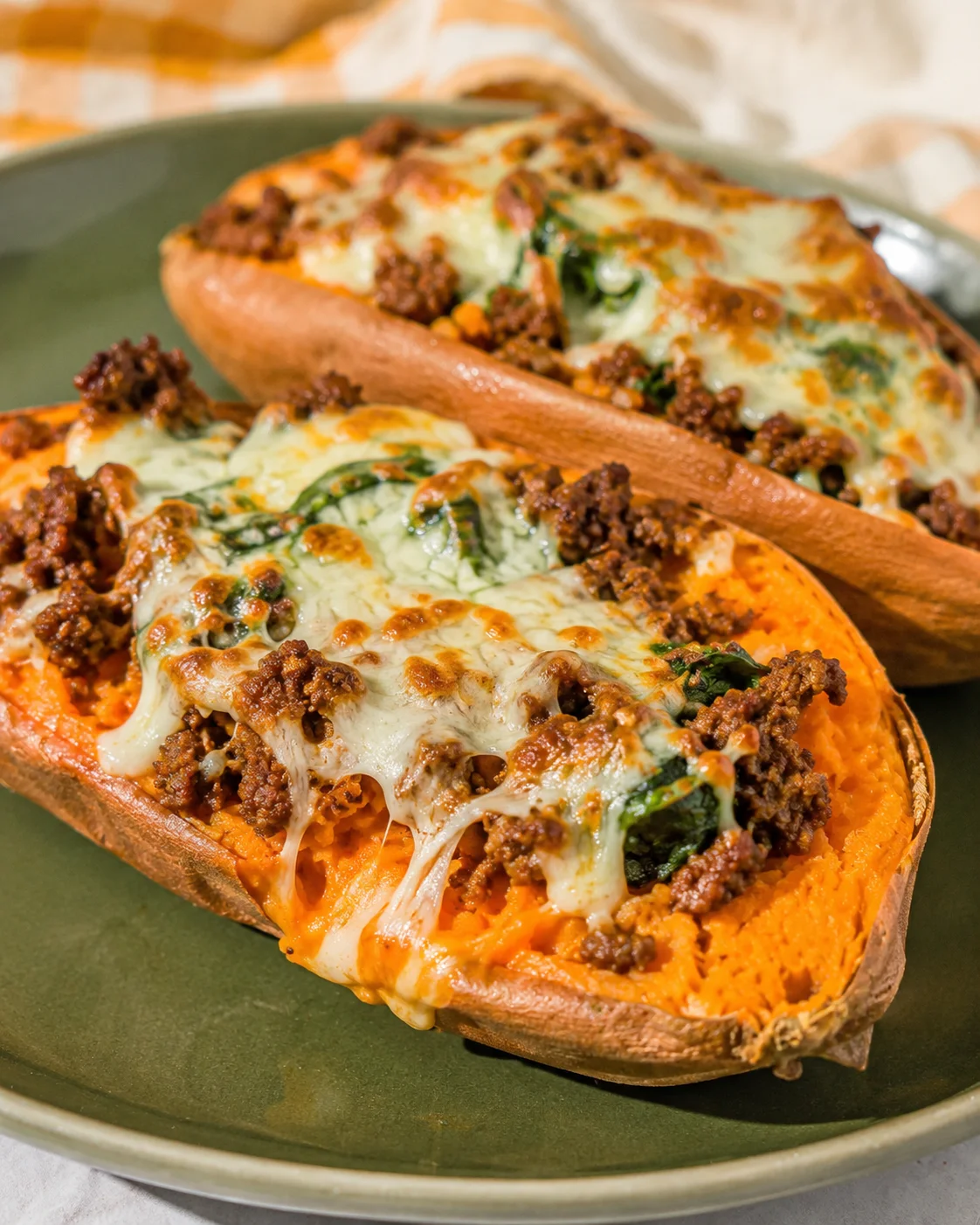 Side view of two stuffed sweet potatoes with gooey melted cheese on a green plate