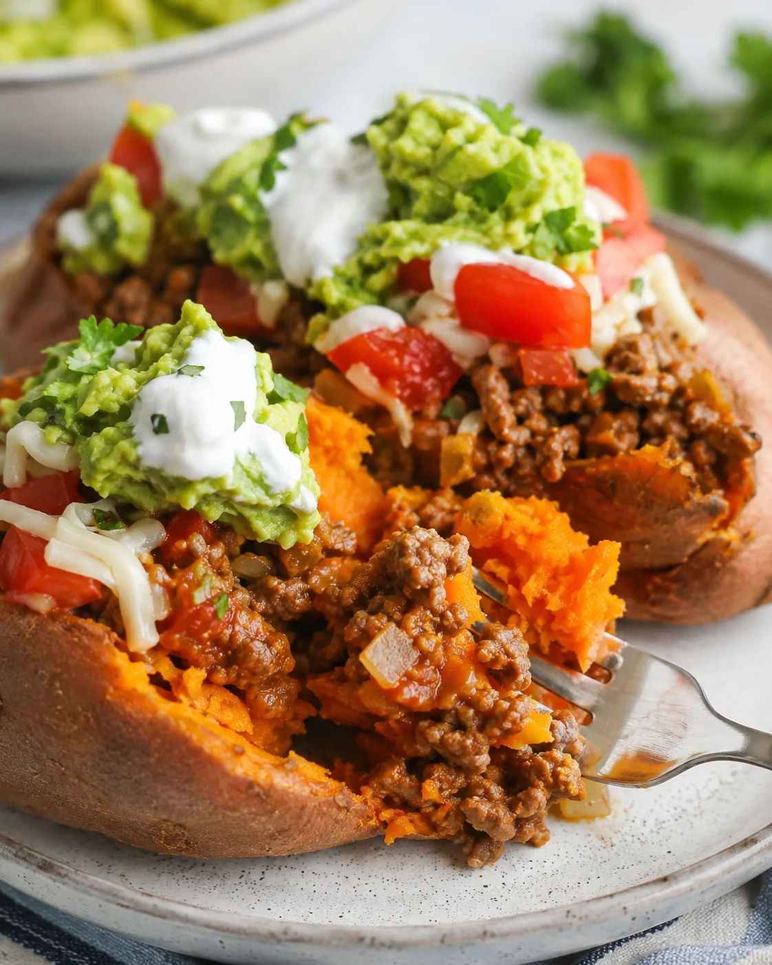 Fork taking a bite from a taco stuffed sweet potato topped with guacamole and sour cream