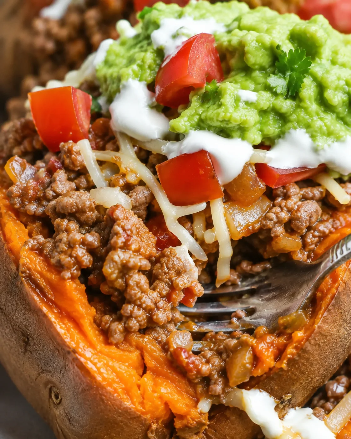 Close detail of the filling in a taco stuffed sweet potato with ground beef, cheese, tomatoes and guacamole
