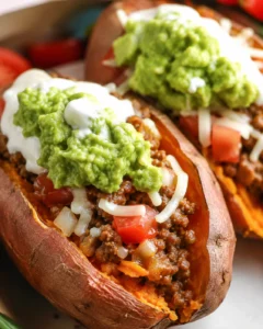 Two taco stuffed sweet potatoes topped with guacamole and sour cream