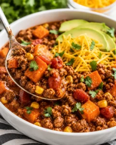 Spoon lifting a portion of turkey sweet potato chili from a bowl topped with avocado and cheese
