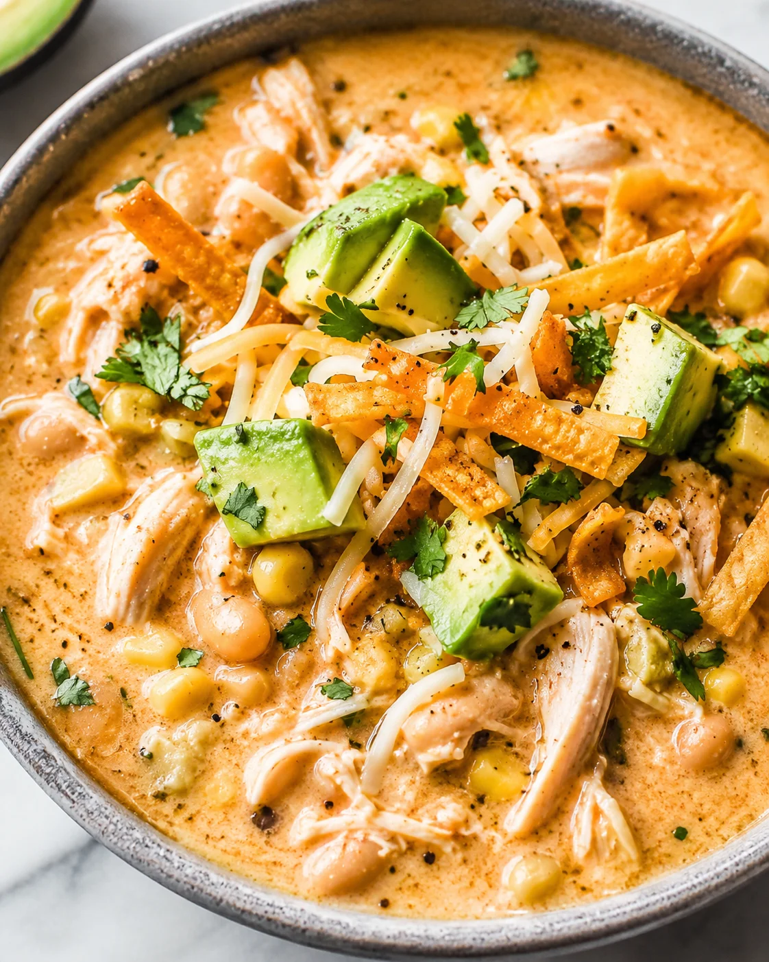 Bowl of white chicken chili topped with avocado, shredded chicken, cheese and tortilla strips